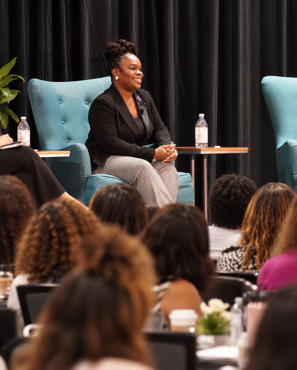 Latisha Newby on stage in a fireside-chat armchair, speaking to a seated audience.